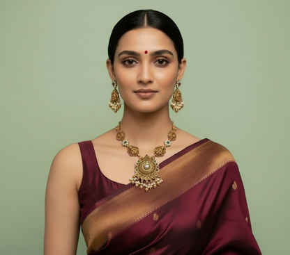 Woman wearing a maroon saree with gold jewelry on a green background