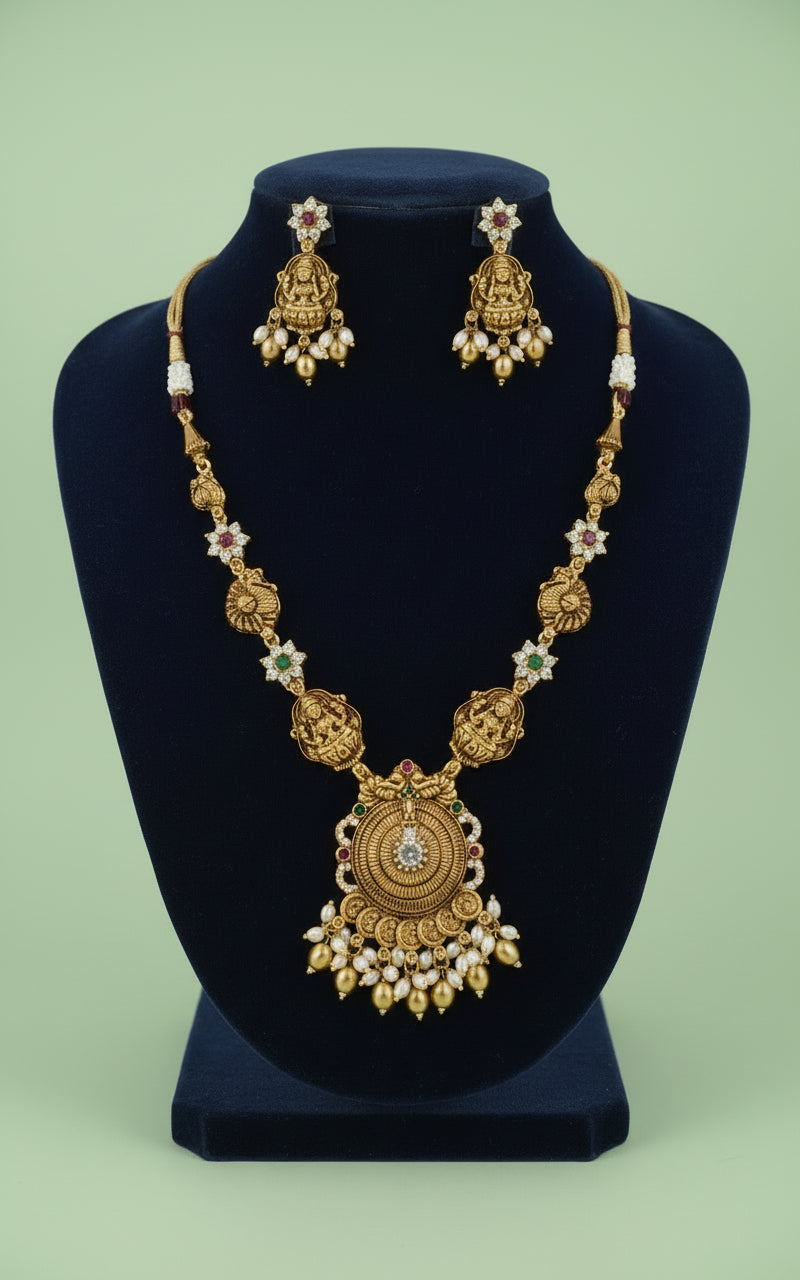 Gold necklace and earrings set on a black stand with a green background