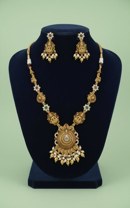 Gold necklace and earrings set on a black stand with a green background