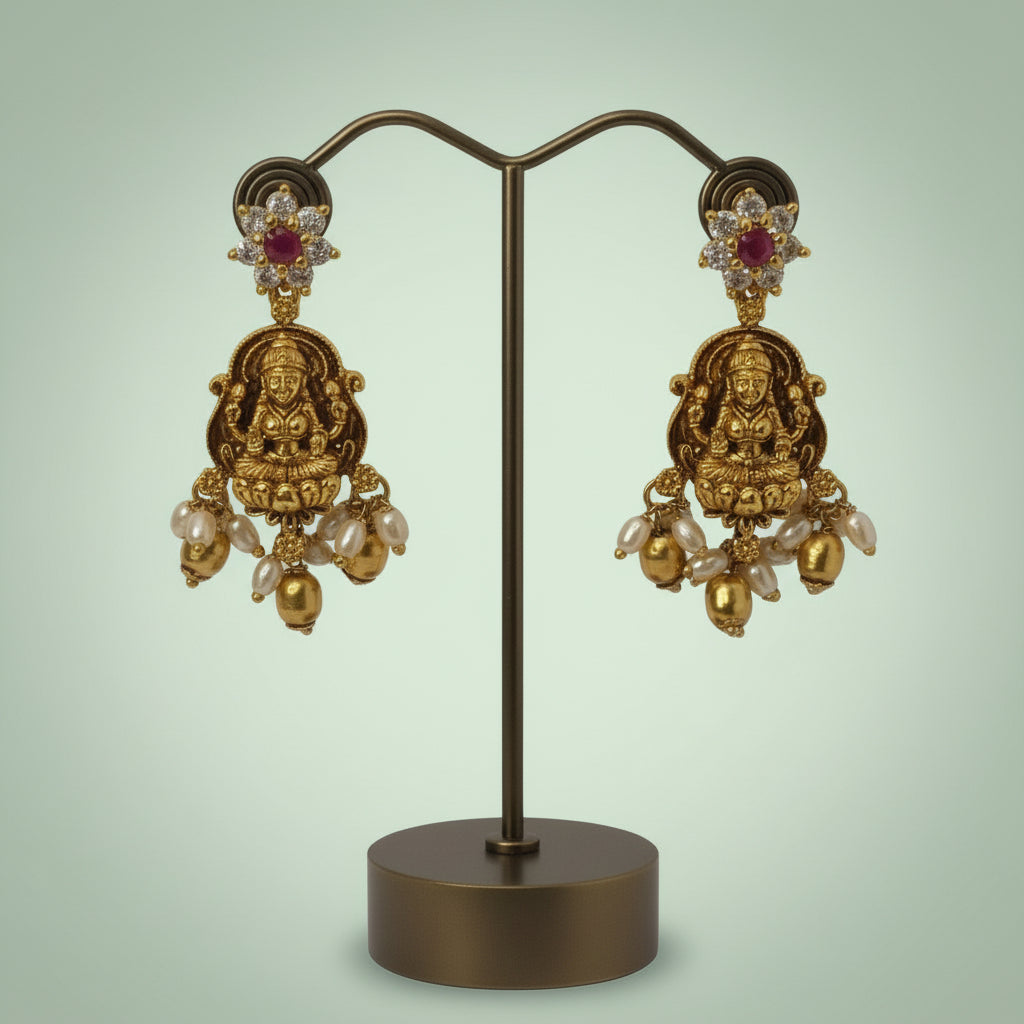 Gold earrings with intricate designs on a stand against a light green background