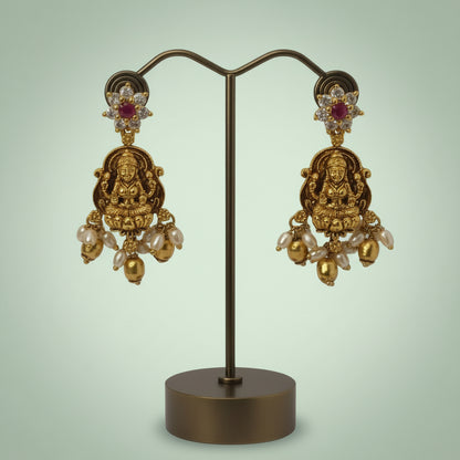 Gold earrings with intricate designs on a stand against a light green background