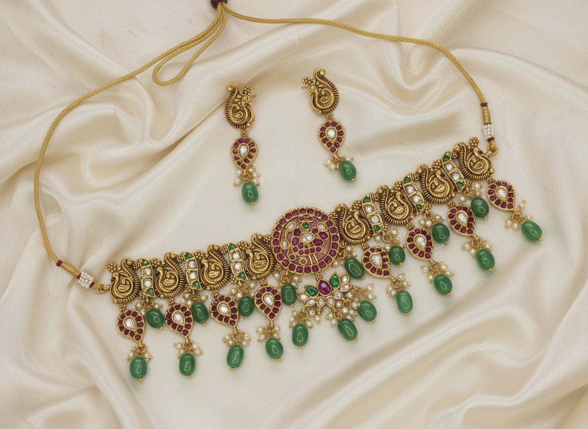 Ornate gold necklace with green and red stones on a beige fabric background