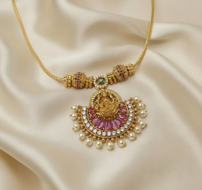 Gold necklace with pink gemstone and pearl details on a purple fabric background