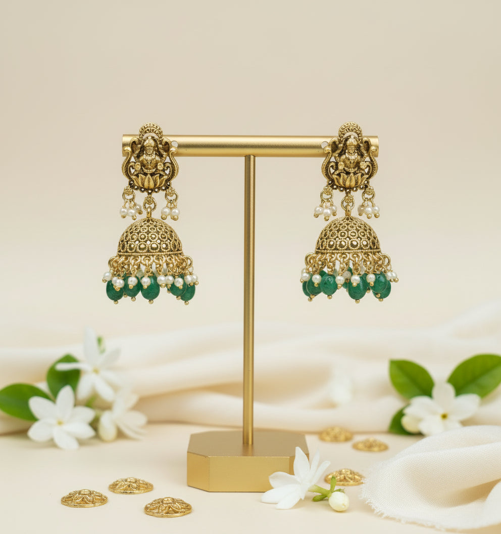 Gold and green earrings on a gold stand with white flowers in the background