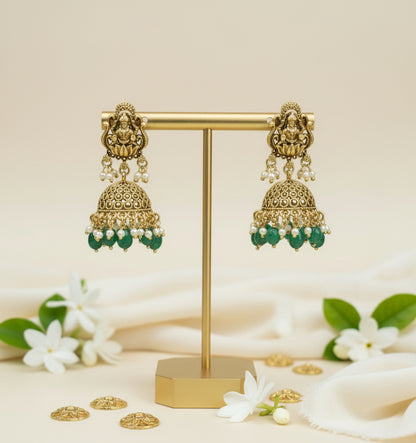 Gold and green earrings on a gold stand with white flowers in the background