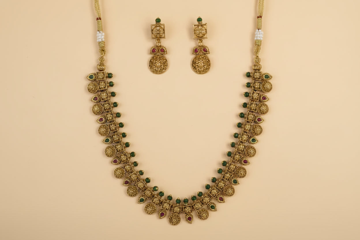 Gold necklace with green stones and matching earrings on a beige background
