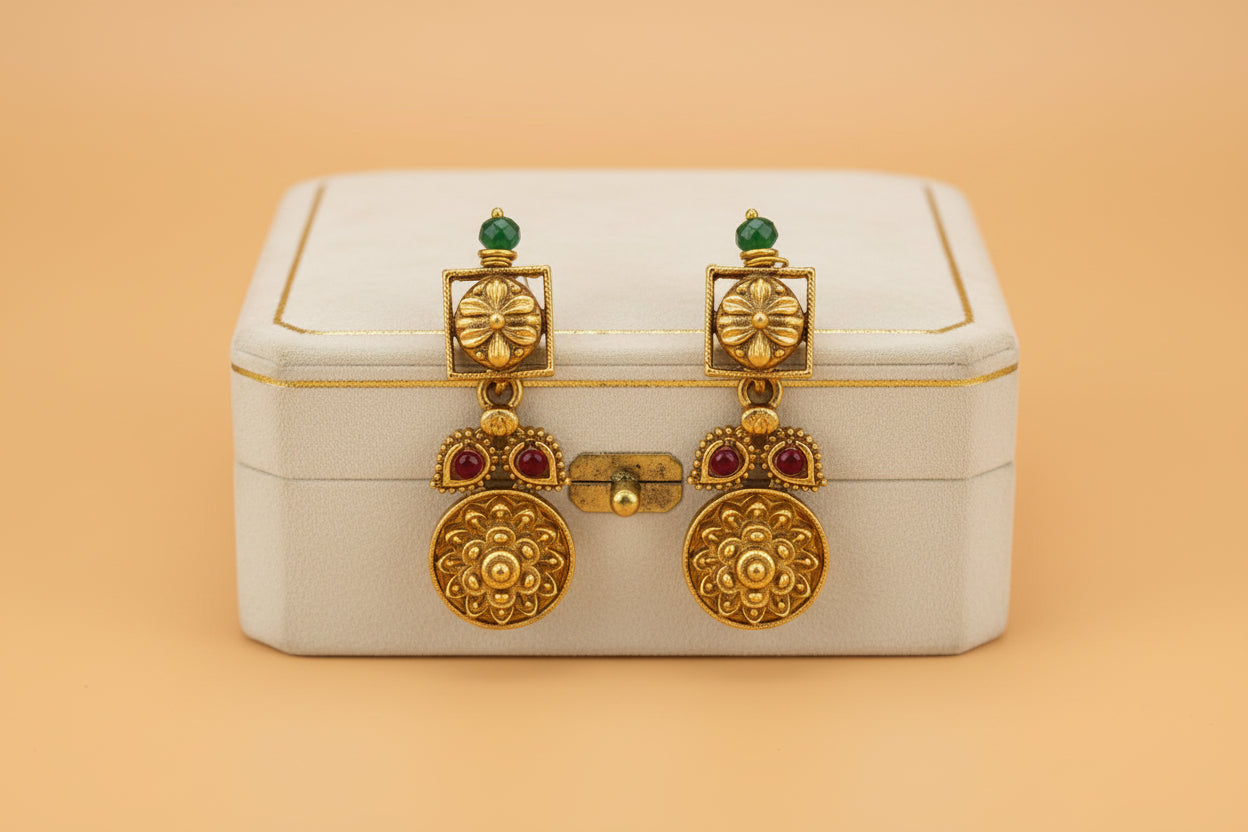 Gold earrings with red stones on a white box against an orange background
