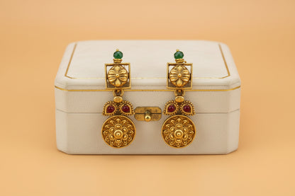 Gold earrings with red stones on a white box against an orange background
