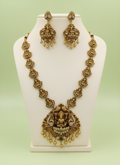 Gold necklace and earrings set on a white stand with a light green background
