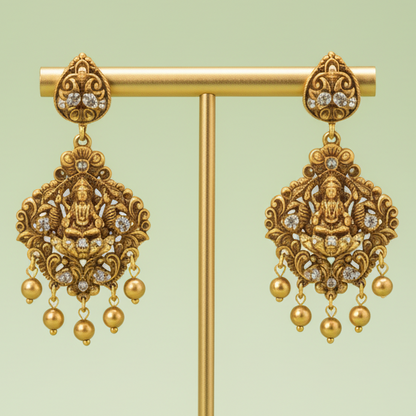 Decorative gold earrings on a matching stand against a light green background