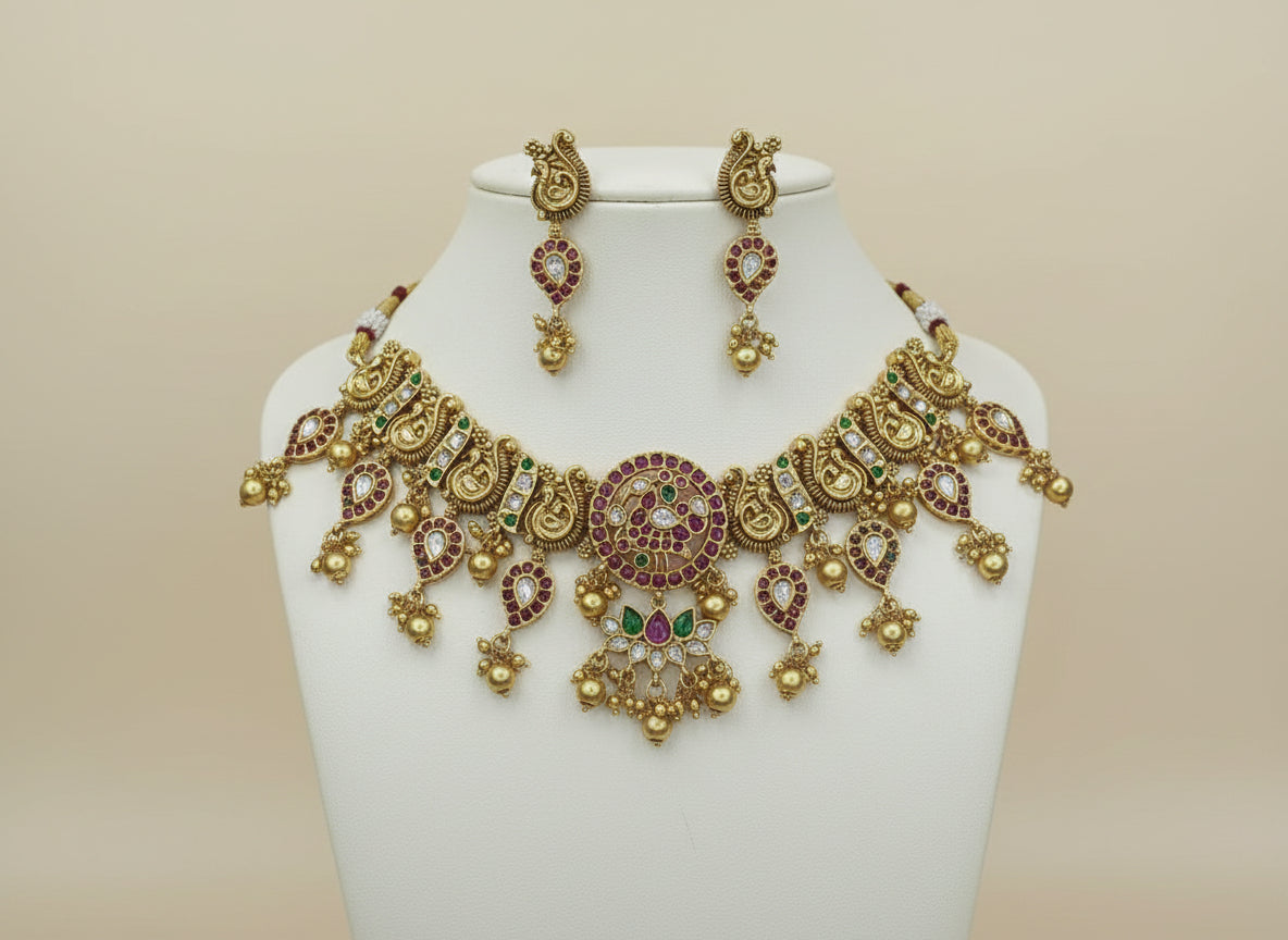 Gold necklace with red and green stones on a white fabric background