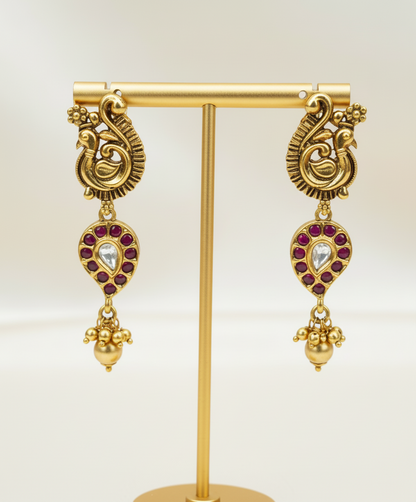 Gold earrings with red stones on a gold stand against a white background