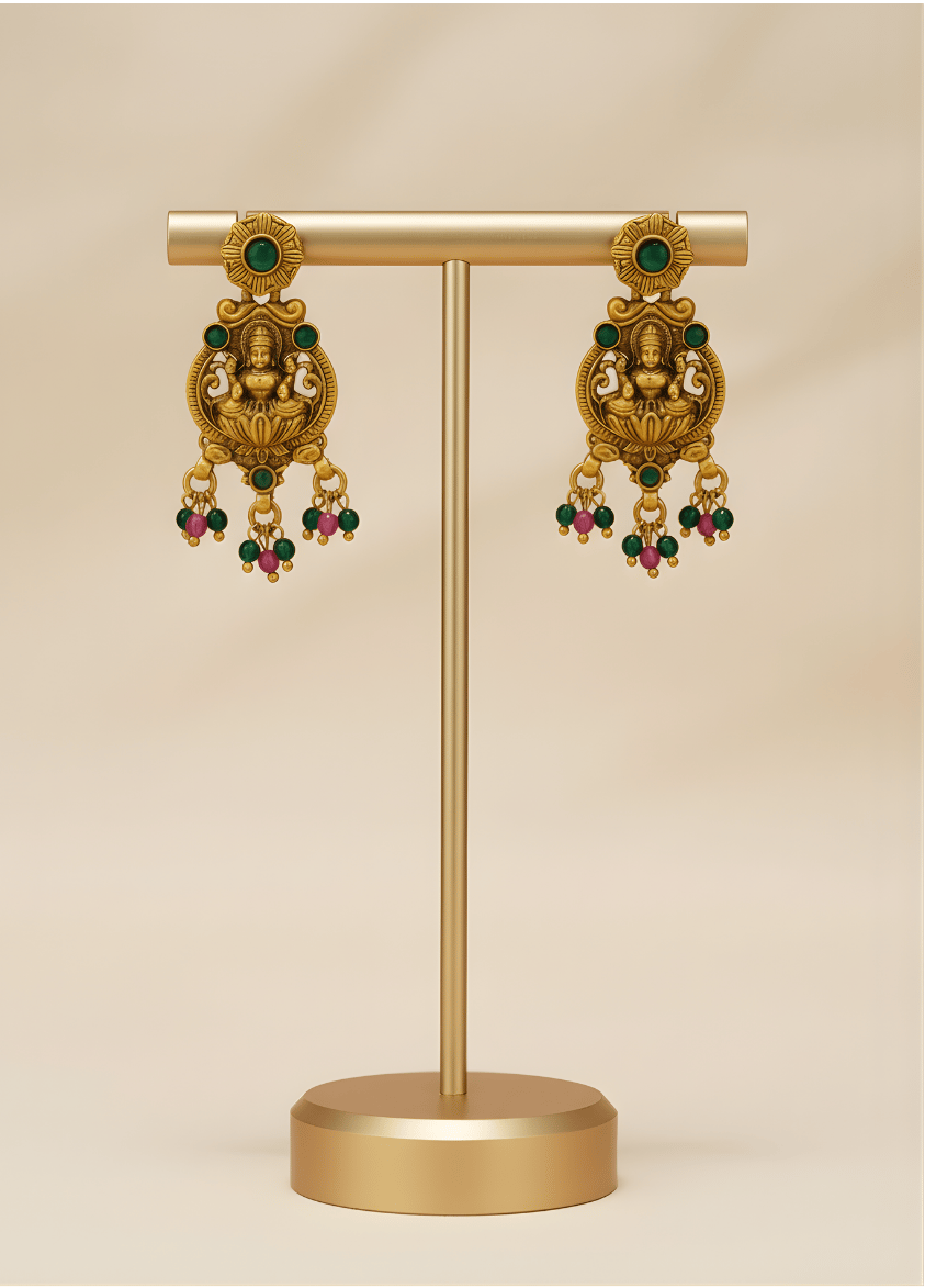 Gold earrings on a stand against a beige background