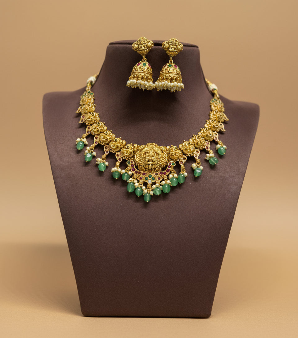 Gold necklace with green beads and matching earrings on a brown stand against a beige background