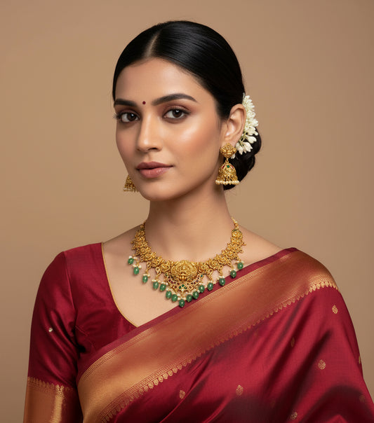 Woman wearing a red saree with gold jewelry against a beige background