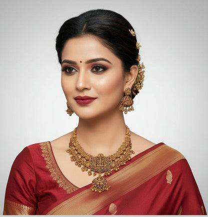 Ornate gold necklace and earrings set with red and green stones on a white background