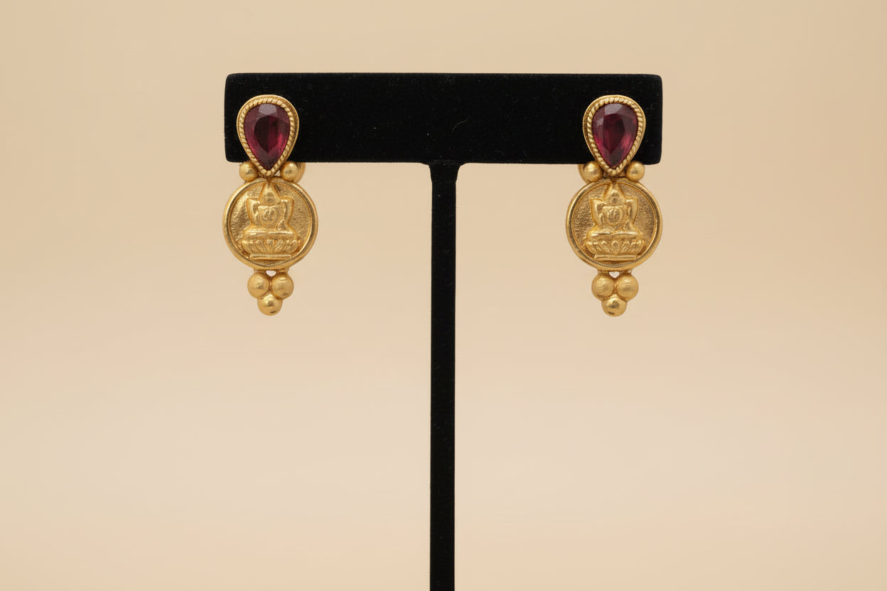 Pair of gold earrings with red gemstones on a light red background