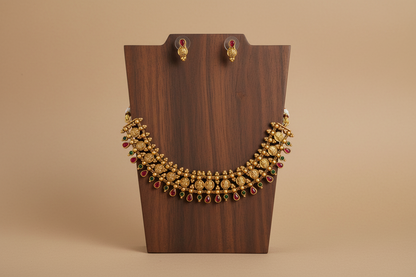Gold necklace with red stones on a wooden stand against a brown background