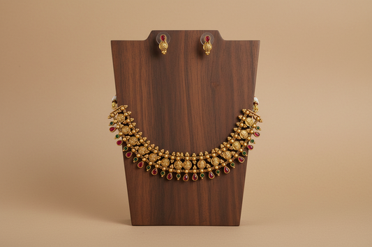 Gold necklace with red stones on a wooden stand against a brown background
