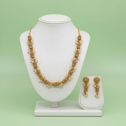 Gold necklace and earrings on a white mannequin bust with a green background