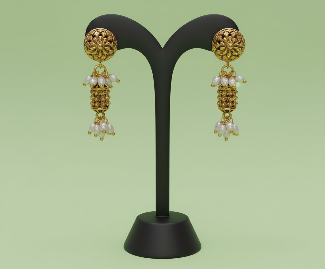 Gold earrings with pearl drops on a black stand against a green background