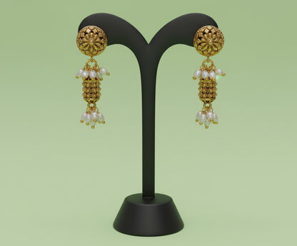 Gold earrings with pearl drops on a black stand against a green background