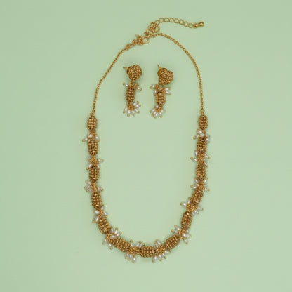 Gold necklace and earrings set on a light green background