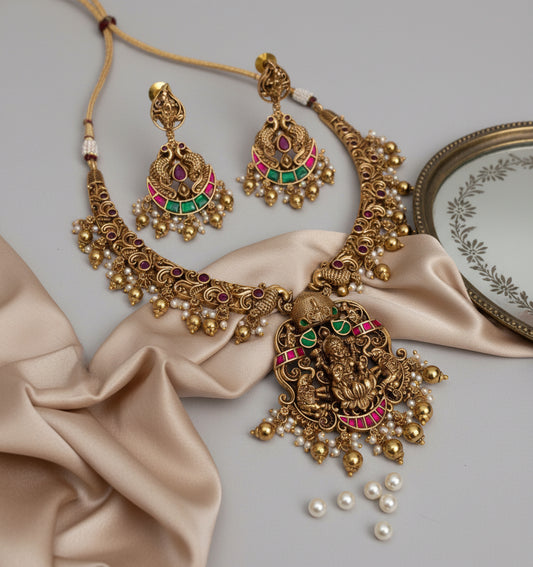 Ornate gold necklace and earrings with stones on a beige fabric background