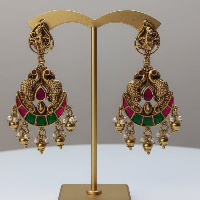 Gold earrings with red and green accents on a gold stand against a gray background
