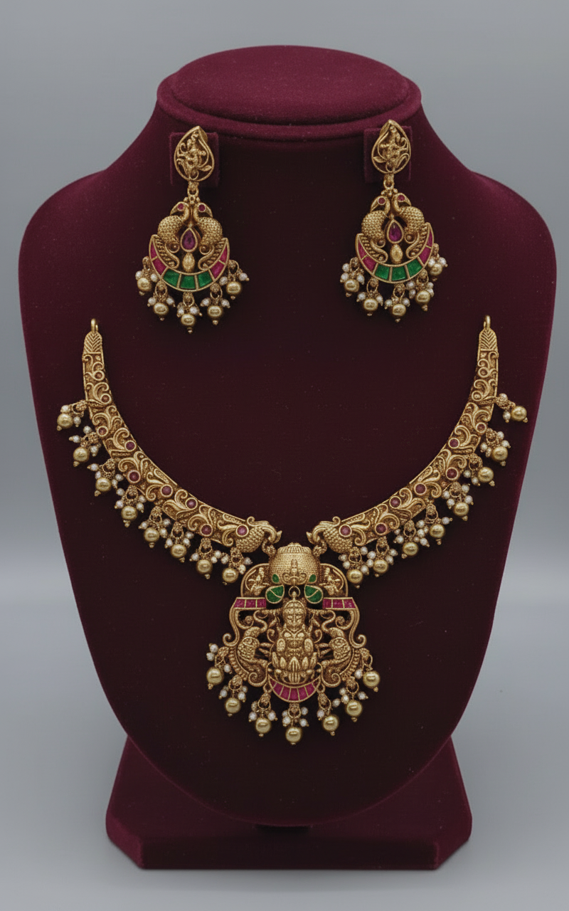 Gold necklace and earrings set on a maroon stand with a gray background