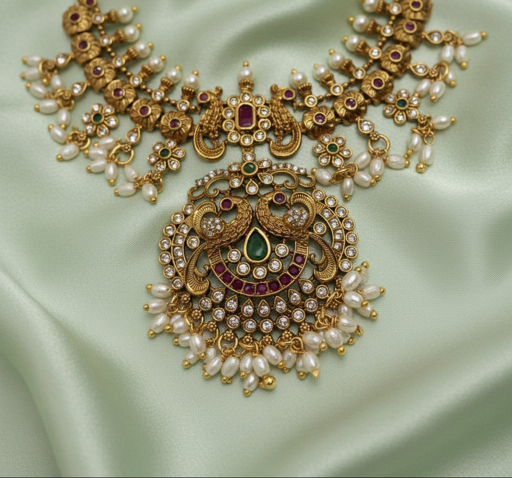 Ornate gold jewelry piece with pearls and gemstones on a light background