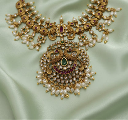 Ornate gold jewelry piece with pearls and gemstones on a light background