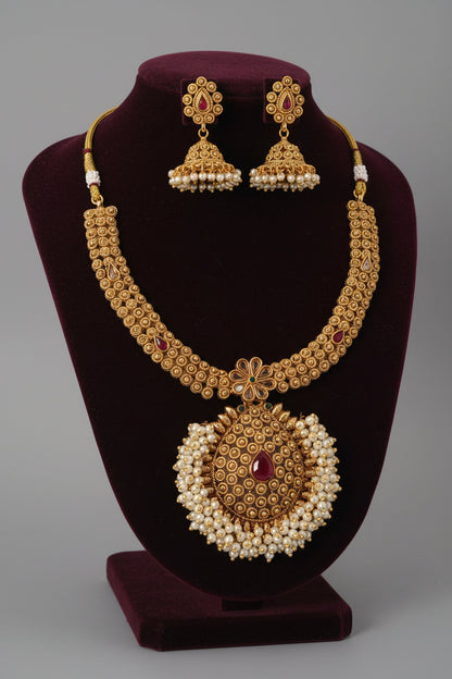 Gold necklace and earrings set on a purple stand against a gray background