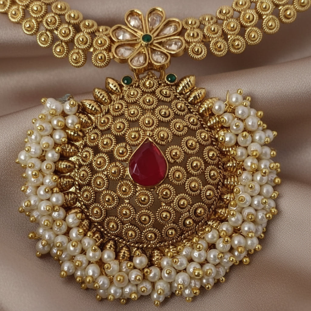 Ornate gold and pearl necklace with a red gemstone on a purple background