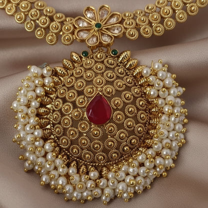 Ornate gold and pearl necklace with a red gemstone on a purple background