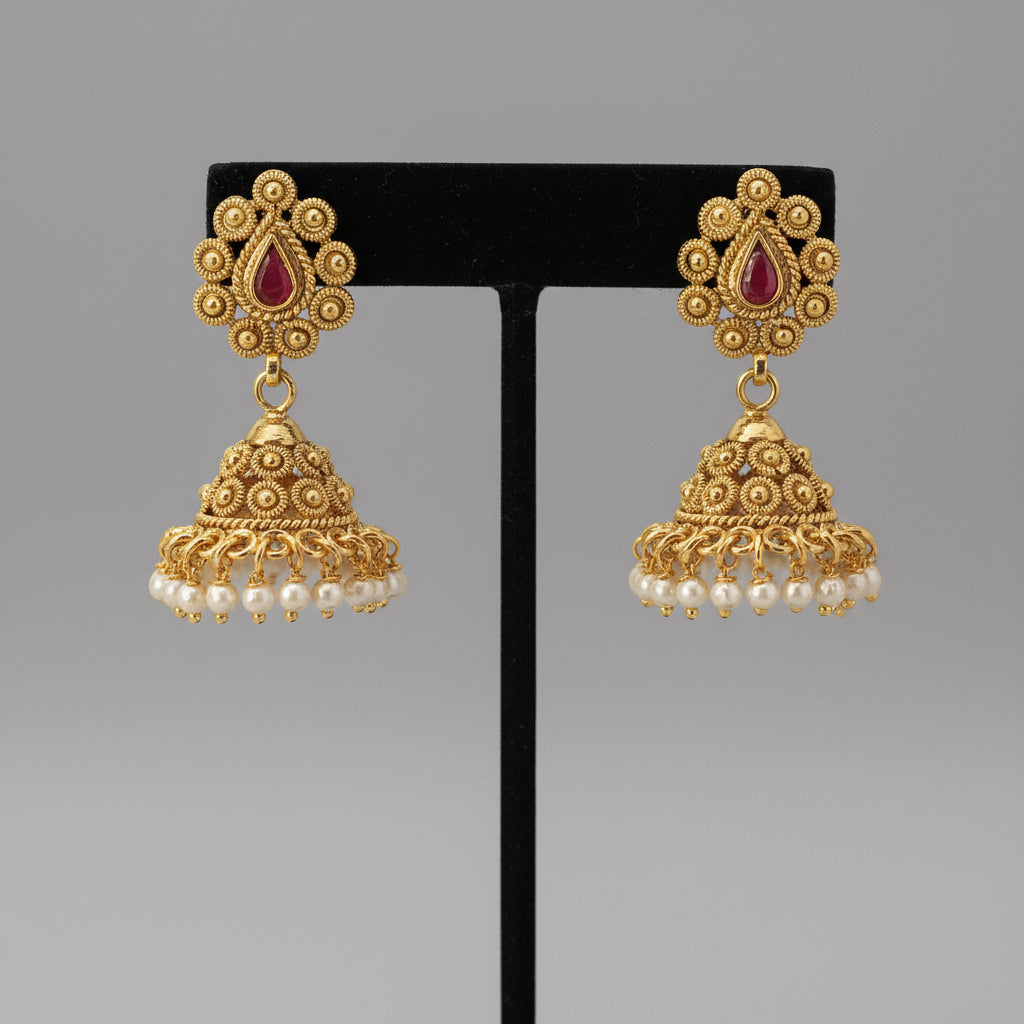 Pair of gold earrings with red stones and pearl drops on a black stand against a gray background