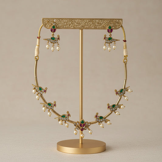 Gold necklace with emeralds and pearls on a gold stand against a beige background