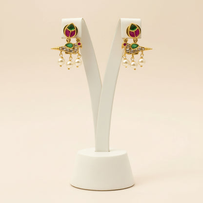 Pair of gold earrings with gemstones on a white stand against a beige background