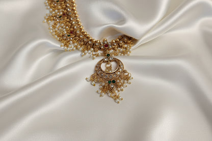 Gold necklace with green gemstones on a white satin background