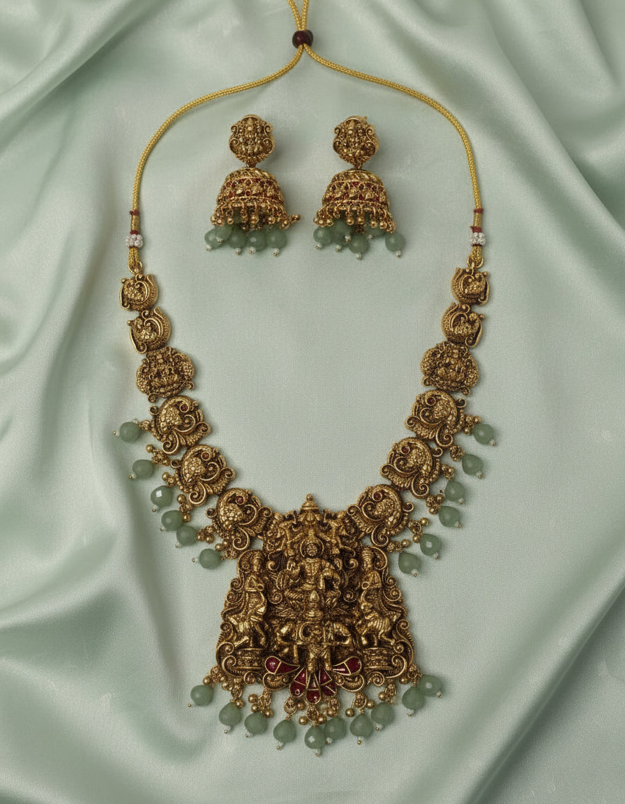 Ornate gold necklace with matching earrings on a light green fabric background