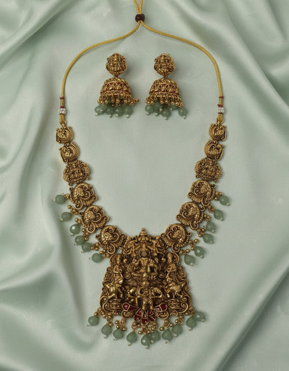 Ornate gold necklace with matching earrings on a light green fabric background