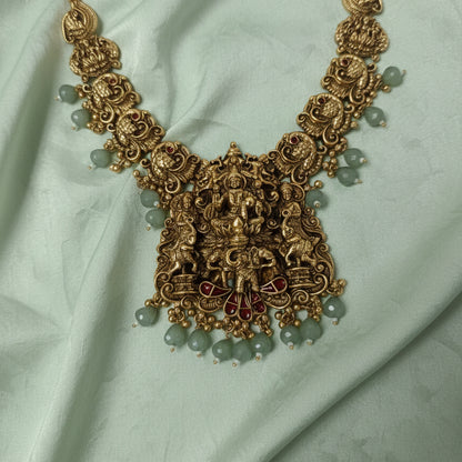 Ornate gold necklace with green beads on a white background