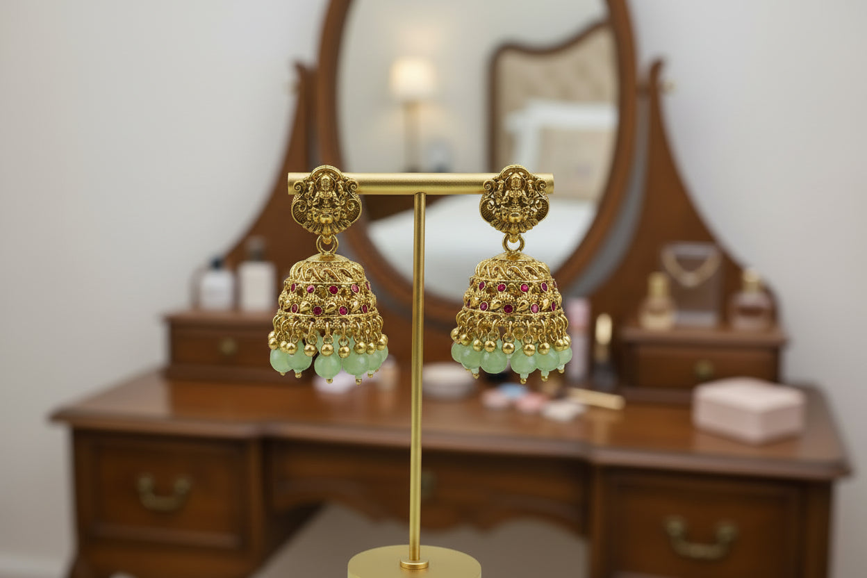 Gold earrings with green beads on a gold stand against a light green background