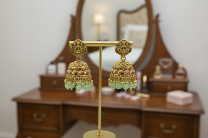Gold earrings with green beads on a gold stand against a light green background