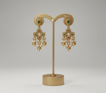 Gold earrings with green stones on a gold stand against a gray background