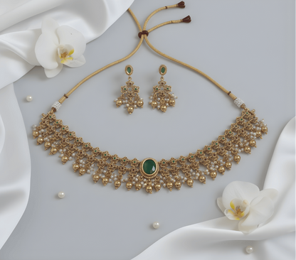 Gold necklace and earrings with green stones on a white fabric background