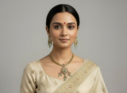 Woman wearing a gold necklace and earrings with a beige saree on a gray background