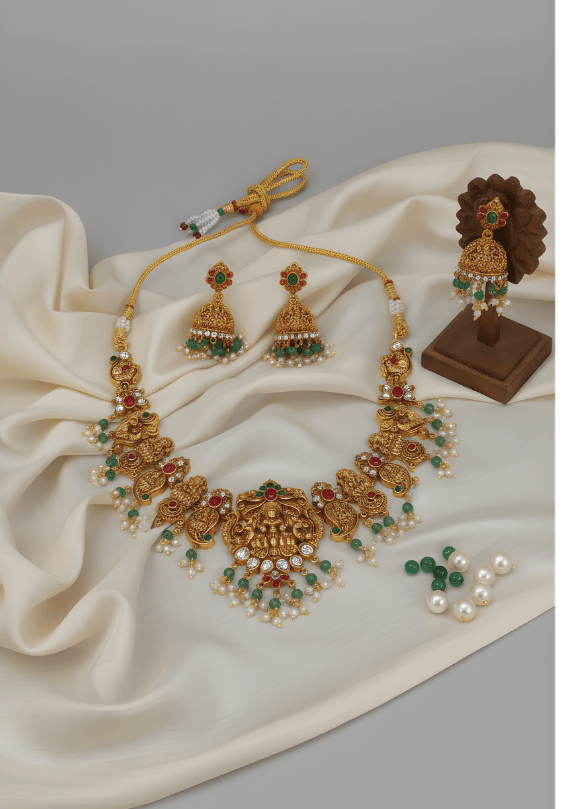 Gold necklace with green and red stones on a white fabric background