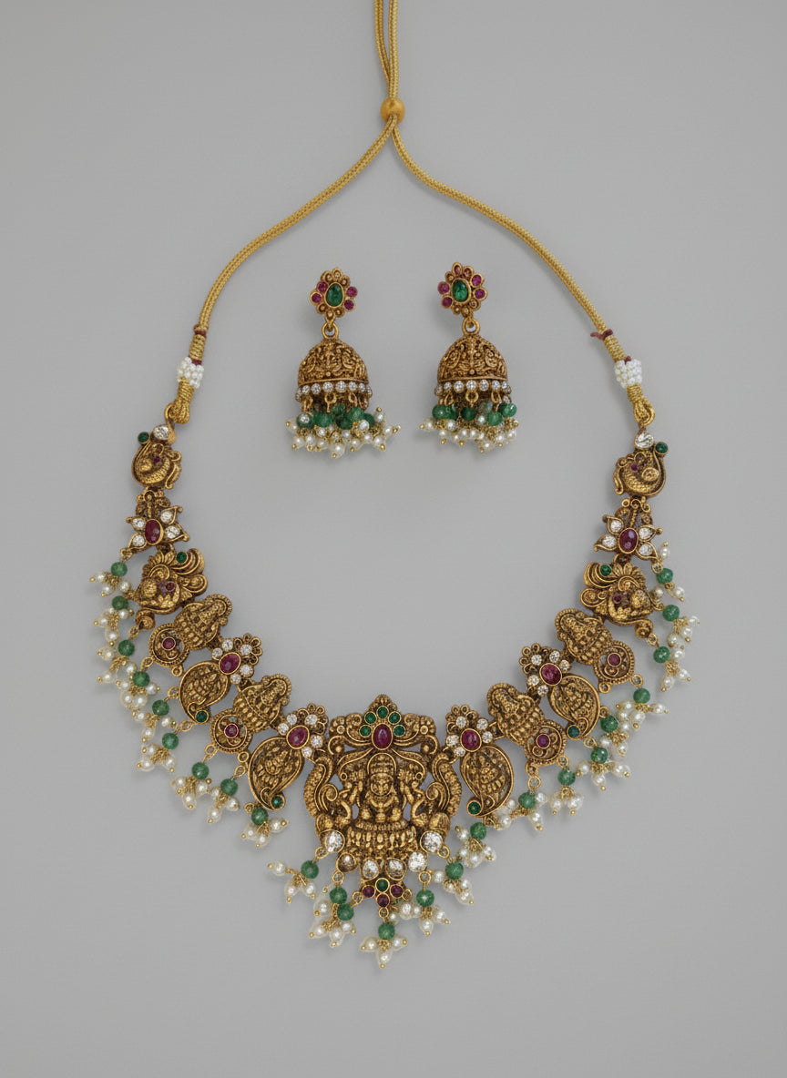 Gold necklace with green and red stones on a gray background