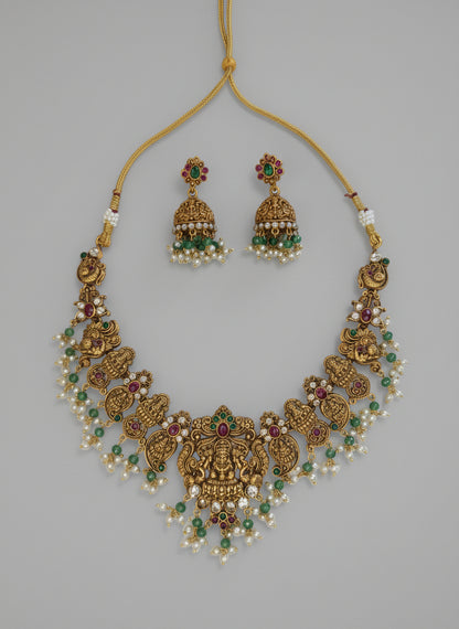 Gold necklace with green and red stones on a gray background